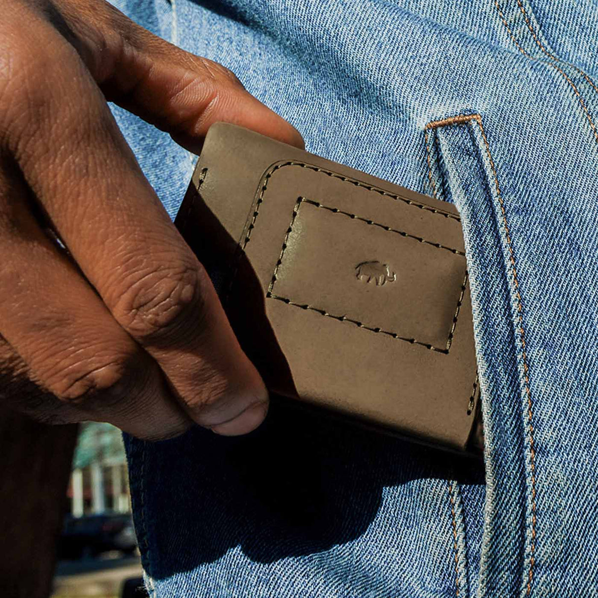 Hand holding a olive leather wallet against blue denim jeans.