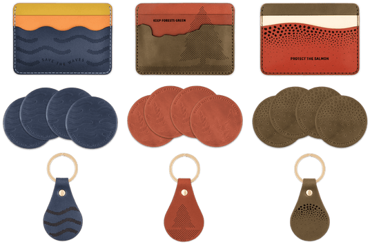 A top down view of the Giveback Collections: Save the Waves, Keep Forests Green, and Protect the Salmon featuring each design's Half Wallet, round leather coasters, and Tab Keychains with brass hardware.
