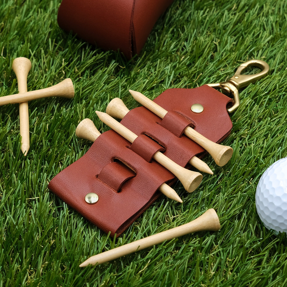 Brown leather Golf Tee Tag on a bed of grass with golf products.
