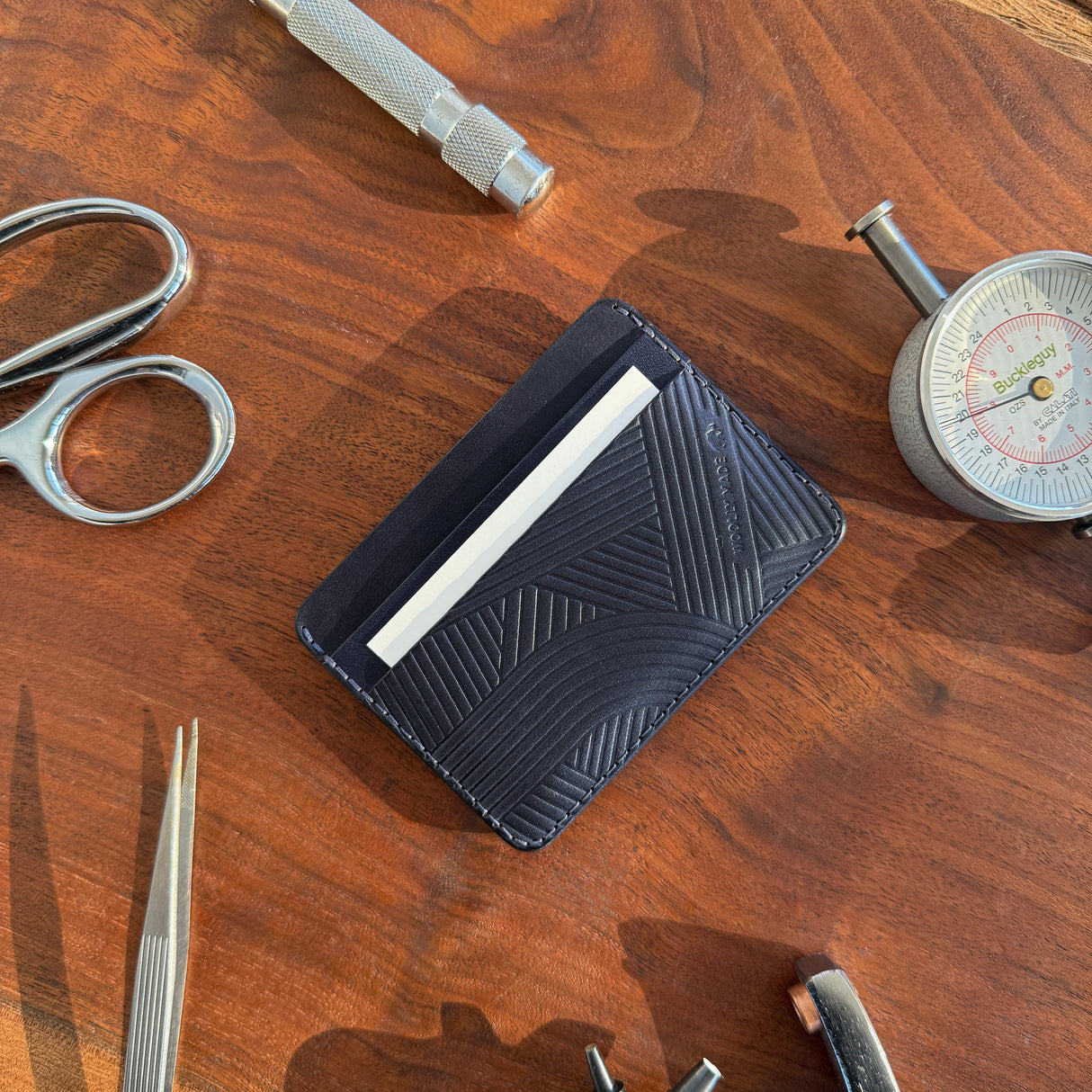 Woolly Made Navy texture line Half Wallet. On a reddish wodden table with leather maker tools surrounding the wallet.