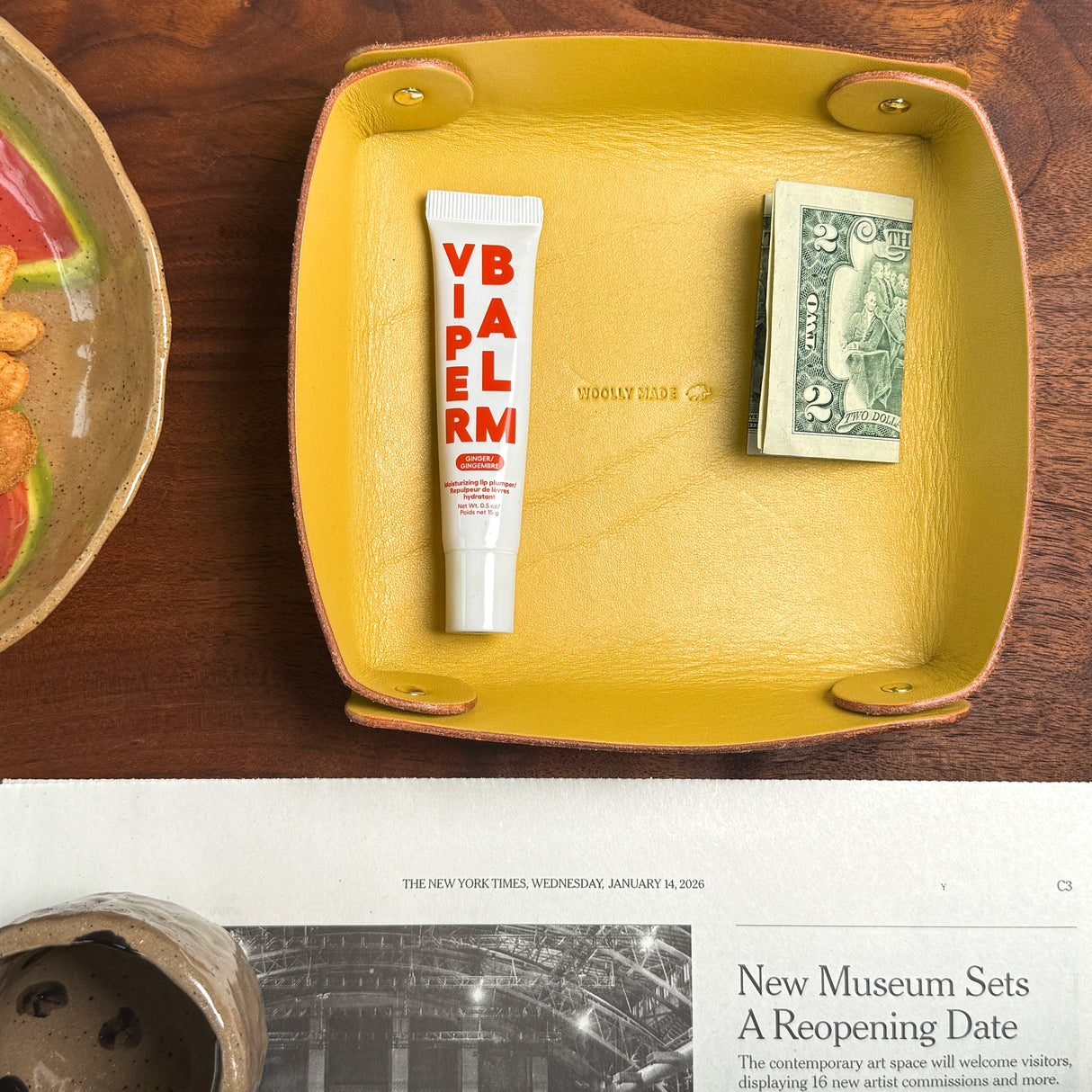 Woolly Made yelow leather Valet Tray on a wooden table with a newspaper and a plate.