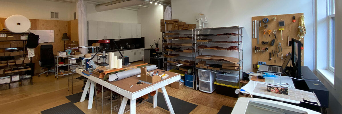 View of the Woolly Made Portland Studio with work benches, tools, shelves, leather hides, and a laser cutter.