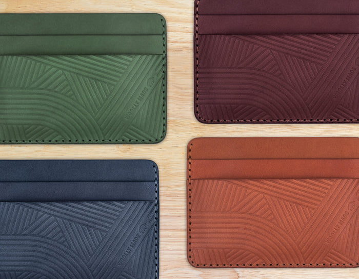 A cropped top down view of the green, burgundy, navy, and brown leather Texture Half Wallets on a wood table.