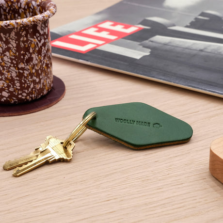 Woolly Made Hotel Keychain in Green on a wooden table with a Hay Design coffee mug and a vintage life magazine.