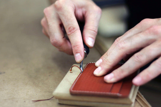 Hands trimming the edges of a brown leather Half Wallet.