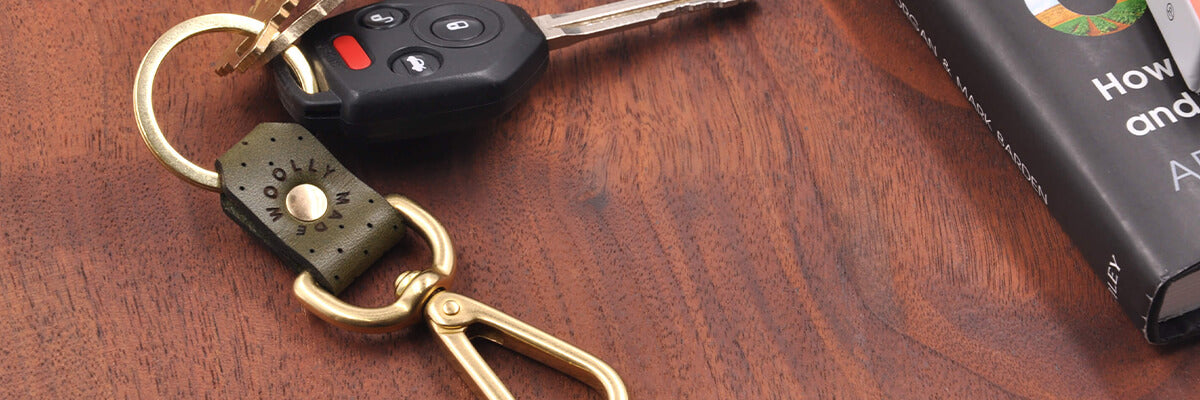 Cropped view of olive leather swivel keychain with brass hardware and keys next to a stack of books.