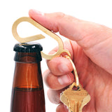 Hand opening a bottle with the Brass Lever Keychain and keys.