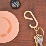 Tod down view of brass Lever Keychain with keys on table with coaster and bottle cap.