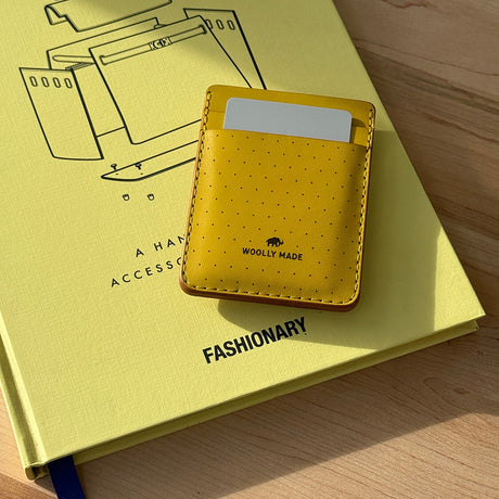 Woolly Made yellow leather money clip wallet displayed on a yellow book.