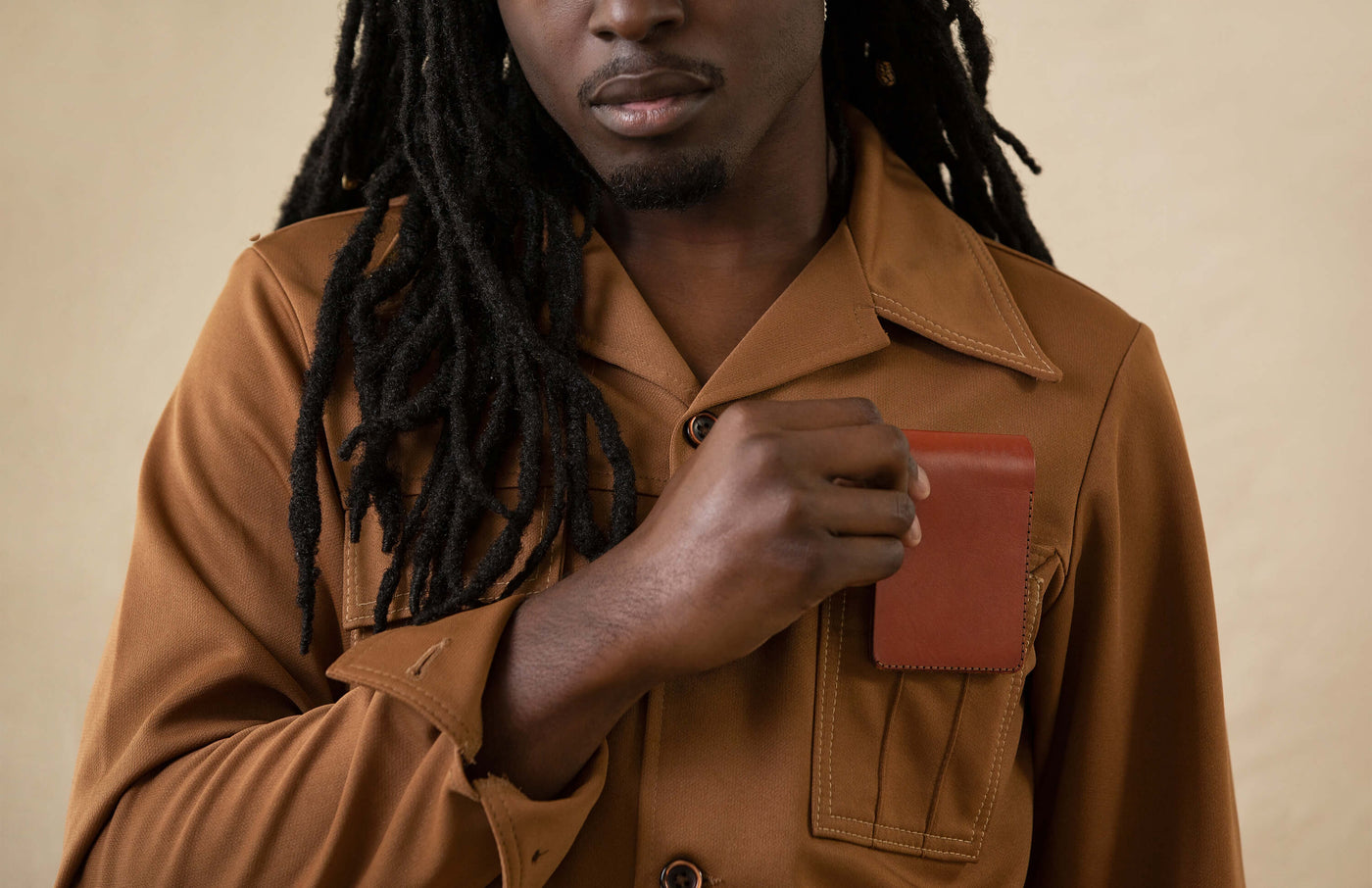 Man putting a folded brown leather Landscape Wallet in his shirt pocket