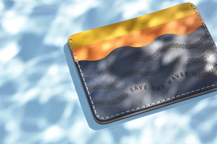 Top down angled view of the yellow, orange, and navy leather Save the Waves Half Wallet with a water like filter effect.