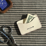 Woolly Made Slim Wallet in Tusk on a green and ivory striped fabric. A $2 bill is coming slightly out of the wallet and a pair of scissors and a wooden tray with Catbird matches are near the wallet.