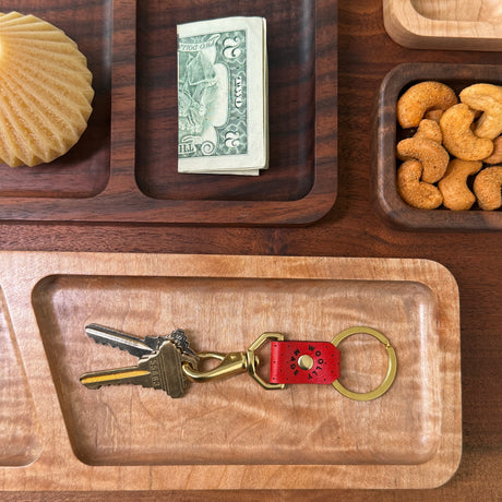 Woolly Made Red leather Swivel Keychain with Brass Hardware. The set is on a table with wooden trays strewn about with little everyday life things surrounding the keychain.
