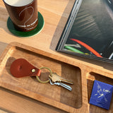Woolly Made Brown Tab Keychain on a wooden table near a Comme Des Garcons Candle and a open magainze.