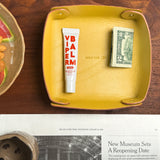 Woolly Made yelow leather Valet Tray on a wooden table with a newspaper and a plate.