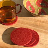 Woolly Made Reddish Brown Coasters on a table with a burnt orange mug with water.