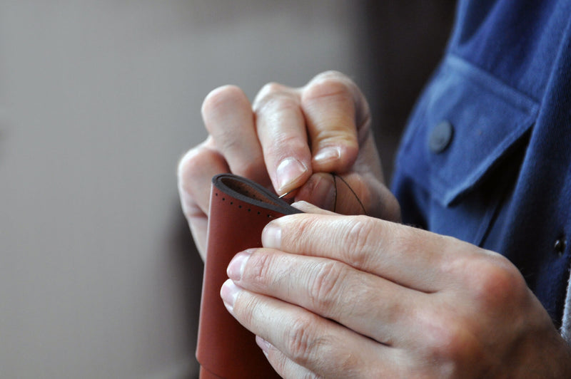 Hands sewing pieces of a leather wallet.