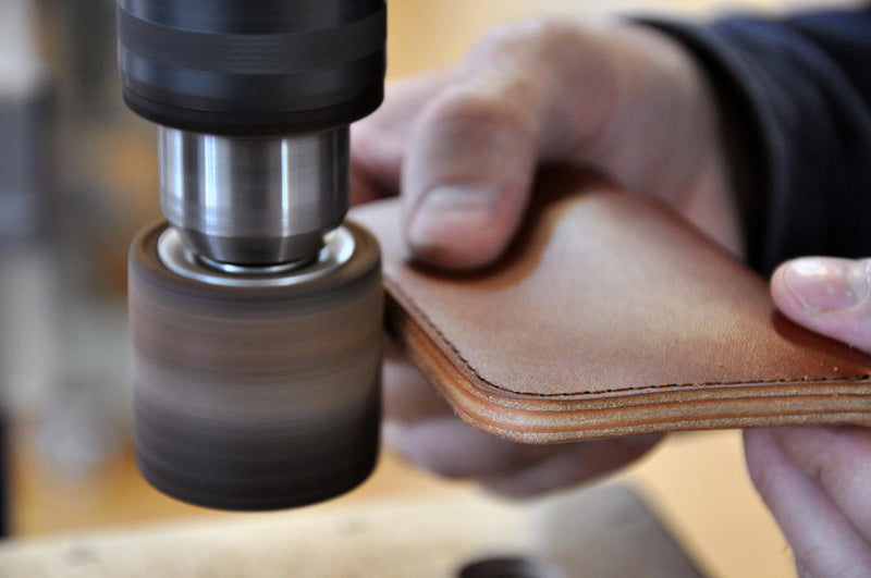 Hands and a tool refining the edge of the assembled wallet.