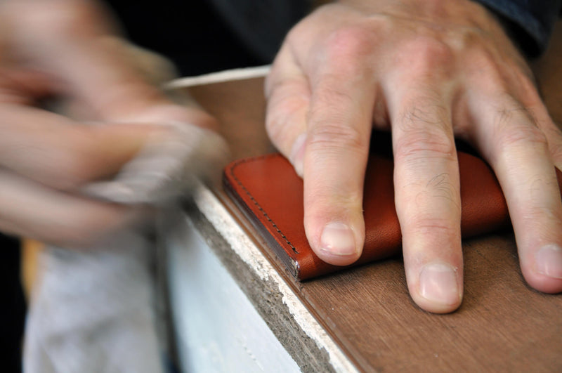 Hands conditioning a leather wallet.