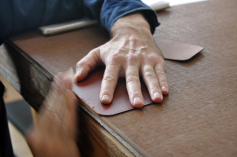 Hands sanding the edge of a leather wallet piece.