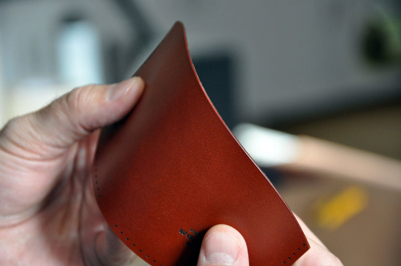 Hands folding a piece of a leather wallet.