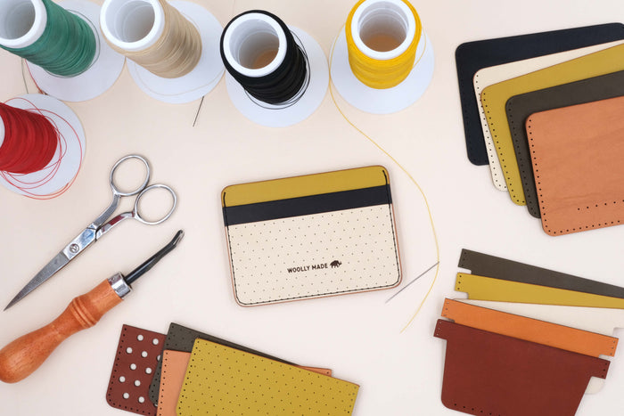 Top down view of wallet making supplies, including leather and thread, plus a yellow, black, and tusk Half Wallet with decorative perforation and the Woollly Made logo.